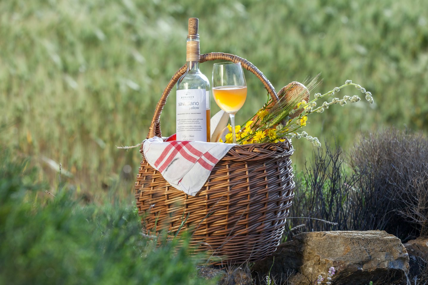 Piknikkurv fylt med vin og markblomster på steiner.