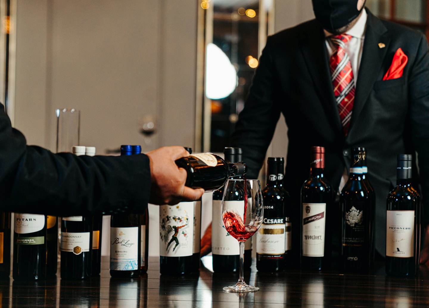 Sommelier heller rødvin i et glass på et bord.